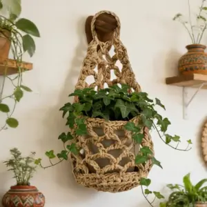 Hängender, geknüpfter Netzkorb in Naturbraun mit grüner Pflanze an einem Holzhaken an der Wand