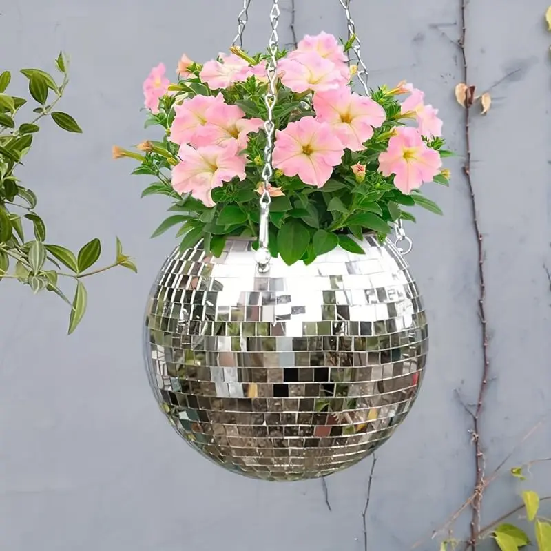 Hängende Spiegelkugel in Silber an Ketten, gefüllt mit rosa Blumen, vor einer grauen Wand